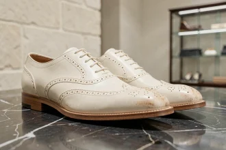 Paire de chaussures Oxford en cuir ivoire de marque de luxe posée sur un marbre noir poli, mettant en valeur la qualité artisanale et le détail des coutures