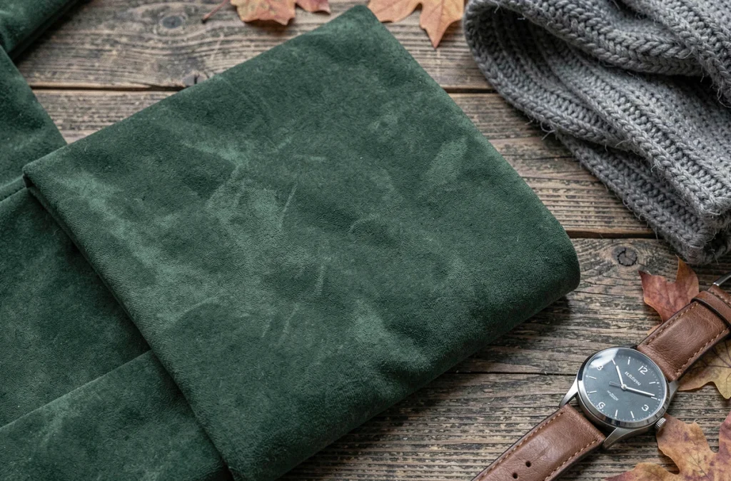 Détail de tissu daim vert forêt plié sur une surface en chêne, accessoires mode automne-hiver 2026